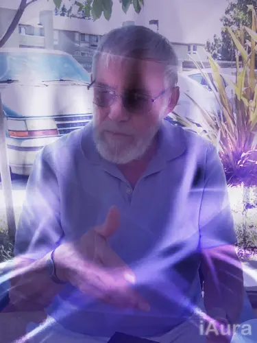 Man wearing sunglasses, seated outdoors with a blurred effect.