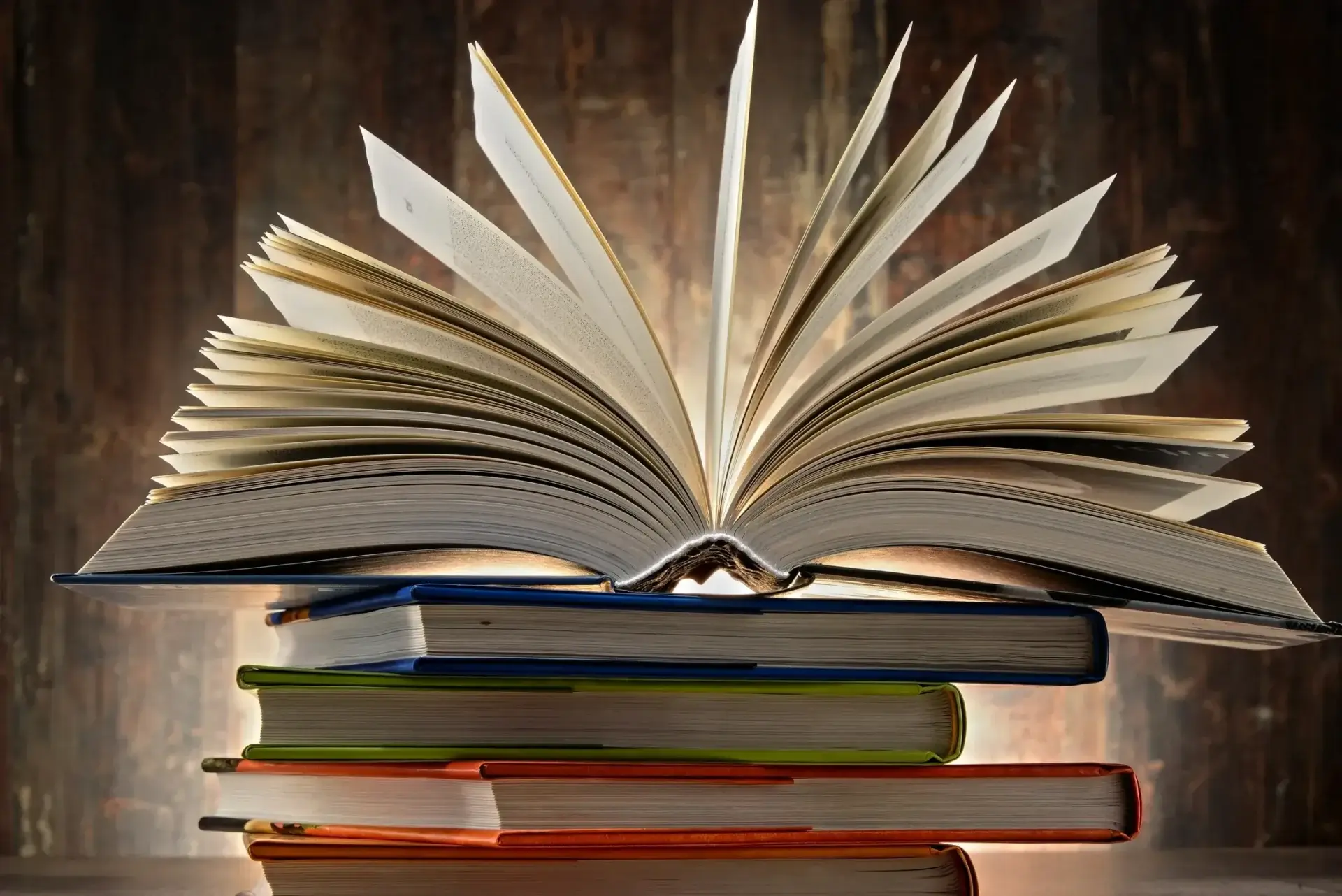A stack of books with an open book on top, pages fanned out.